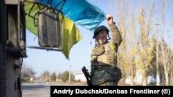 A soldier holds a weathered Ukrainian flag as the sun begins to set on the freshly recaptured town of Snihurivka, near Kherson.