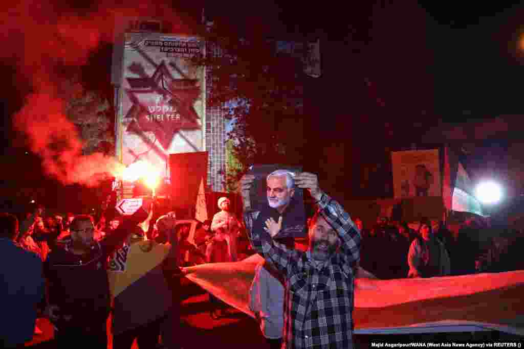 Un bărbat iranian ține în mână un afiș cu comandantul militar iranian, generalul Qassem Soleimani, în timpul sărbătorii stradale de după atacul IRGC asupra Israelului. Soleimani a fost ucis într-o lovitură cu dronă americană lângă Aeroportul Internațional Bagdad, pe 3 ianuarie 2020, în timp ce călătorea pentru a se întâlni cu premierul irakian Adil Abdul-Mahdi.