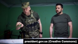 Comandantul forțelor terestre ucrainene, generalul-colonel Oleksandr Sîrski (stânga), îi raportează președintelui Volodimir Zelenski aflat în vizită în apropierea liniei frontului din regiunea Donețk, 26 iunie.