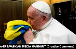 Папа Римський Франциск цілує прапор України зі знищеного армією РФ українського села, який йому подарували разом і браслетом із металу з «Азовсталі» та пачкою солі з останньої партії комбінату «Артемсіль»