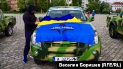Руснак разпъва флаговете на Легион "Свободна Русия" и на Украйна на капака на подготвен за фронта джип.