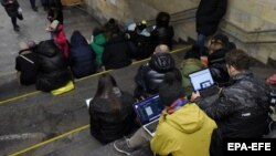 Луѓето ги проверуваат своите уреди за информации во станицата на метрото во Киев за време на воздушен напад, март 2023 година (архивска фоторафија)