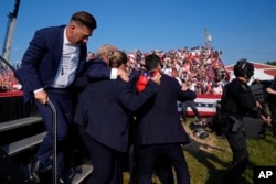 Donald Trump este înconjurat de agenți ai Serviciului Secret al SUA, în timp ce este evacuat, 13 iulie 2024. Înainte să se urce în autovehicul, fostul președinte s-a întors spre mulțime și a ridicat pumnul în aer.