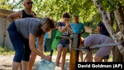 Жителите се собираат да испумпаат вода од бунар надвор од станбен комплекс во Славјанск.