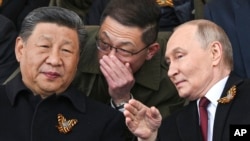 Președintele Federației Ruse Vladimir Putin și liderul Republicii Chineze Xi Jinping discută în timp ce urmăresc parada militară de Ziua Victoriei de la Moscova, la 9 Mai 2025.