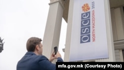 Министерот за надворешни работи Бујар Османи го фотографира банерот врз зградата на МНР поставен во рамки на преземањето на претседавањето со ОБСЕ, 12 јануари 2023 година
