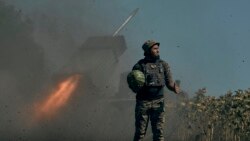 Un soldat ucrainean ține un pepene verde și ridică degetul mare în timp ce rachetele sunt lansate spre linia frontului în regiunea Donețk, estul Ucrainei. 