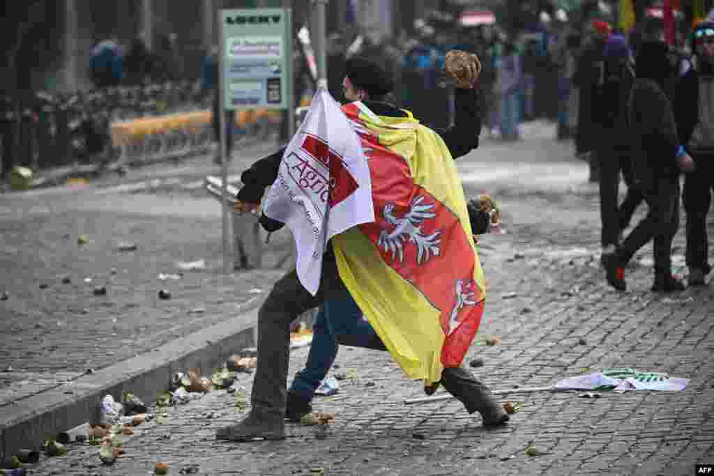 Un tânăr înfășurat în steagul JA (Tinerii Agricultori) aruncă cu legume în sediul Parlamentului European în timpul unui protest al fermierilor pentru a denunța reformele Politicii Agricole Comune (PAC) și acordurile comerciale precum Mercosur, la Bruxelles, 18 decembrie 2025.