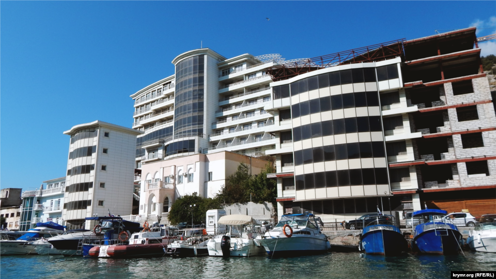 З катера видно багатоповерховий будинок, місцеві називають його пам'ятником &laquo;жадібності століття&raquo;. Капітан судна пояснює, що за проєктом це повинен був бути готель заввишки в три поверхи, але забудовник змінив план і звів десятиповерховий будинок. Через недотримання норм, будівля тріснула і почала розвалюватися. Готель так і не запустили в експлуатацію