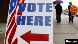 Люди идут мимо указателя пункта голосования. Иллюстративное фото.   