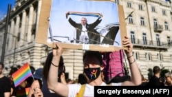 Протестиращ в Будапеща държи снимка, изобразяваща Виктор Орбан, който вдига шал с цветовете на дъгата