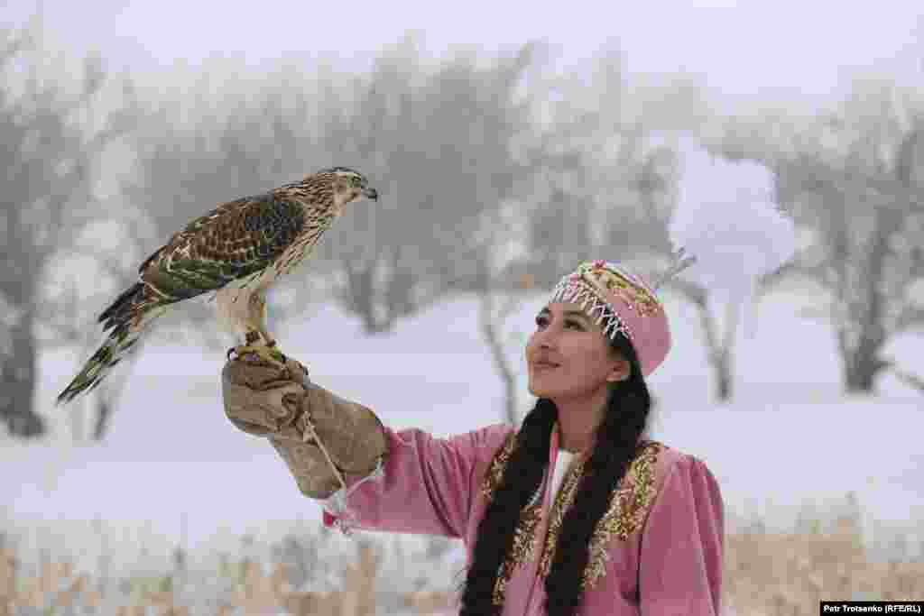 Млада жена в казахстанска народна носия държи ловен сокол по време на състезанието.