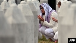 Două femei se roagă la mormintele rudelor lor la cimitirul memorial din satul Potocari, lângă orașul Srebrenița, în estul Bosniei, pe 9 iulie 2025.