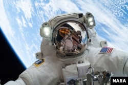 Астранаўт NASA Майк Хопкінс праводзіць касьмічны выхад, каб замяніць няспраўны помпавы модуль на Міжнароднай касьмічнай станцыі. У яго візірку адлюстроўваецца яго калега-астранаўт Рык Мастракіа. Помпа кантралюе паток аміяку для зьнешняй сыстэмы асуджэньня станцыі. 24 сьнежня 2013