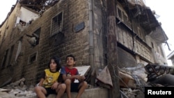 Сириянын Хомс шаарындагы талкаланган үйдүн жанында отурган балдар