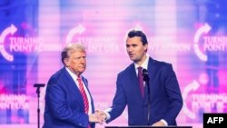 Activistul de dreapta Charlie Kirk (dreapta) vorbește pe scenă cu președintele Donald Trump la America Fest 2024 din Phoenix, Arizona, pe 22 decembrie 2024.