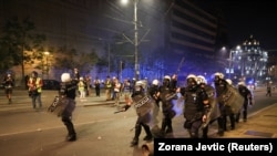 Новинари со шлемови и гас-маски зад полицајци на протест во Белград, Србија, 15 август 2025 година.