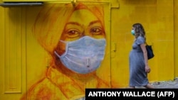 Беременная женщина в защитной маске проходит мимо уличной росписи в Гонконге. 23 марта 2020 года.
