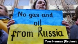 Žena na protestu u Briselu ispred nemačke ambasade drži transparent tokom demonstracija podrške Ukrajini, 11. mart 2022.