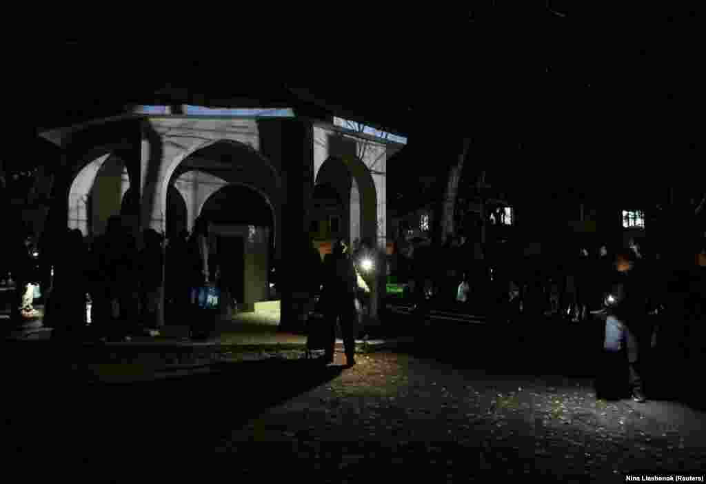 Через російські атаки у більшій частині Одеси немає також водопостачання. На фото: жителі Одеси користуються ліхтариками, стоячи в черзі, щоб наповнити пляшки свіжою питною водою. Одеса, 13 грудня 2025 року