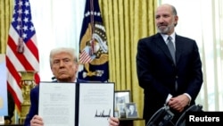 Președintele american Donald Trump arată un ordin executiv privind creșterea tarifelor, flancat de secretarul american al comerțului, Howard Lutnick, în Biroul Oval al Casei Albe din Washington, D.C., SUA, 13 februarie 2025.