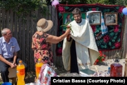 O femeie dăruiește flori unui preot în timpul ritualului de resfințire a Fântânii lui Florescu, construită de Haralambie, în cadrul zilelor deschise „Fântânile Sudului”.