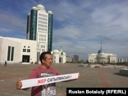 Активист Галымбек Акулбеков стоит в центре Астаны с плакатом, призывающим не продавать землю. Астана, 20 апреля 2016 года.