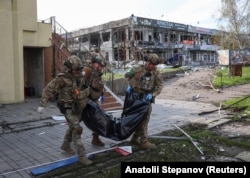 Полицейские несут тело человека, убитого в Покровске, 12 апреля 2025 года