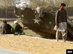 Мужчины-афганцы сушат рис у разбитого бронетранспортера , 15 ноября 2001 года. Иллюстративное фото.