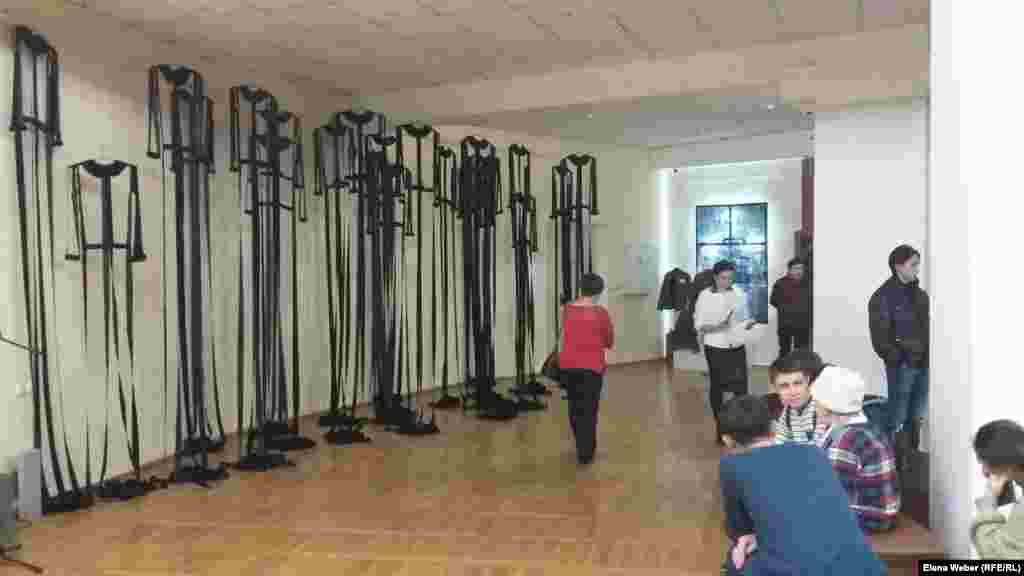 Эта инсталляция "АЛЖИР" посвящена 18 тысячам узниц Акмолинского лагеря жен изменников родины. Не все посетители сразу понимали, что это, но приглядевшись, видели силуэты женских платьев. Образ длинных лагерных черных балахонов-платьев, от которых остались лишь швы, воротнички и манжеты, выбран автором не случайно. По задумке Айнур Саденовой, несмотря на потерю семьи, нечеловеческие условия в лагерях и физическую надломленность, узницы оставались женственными, добрыми и интеллигентными.