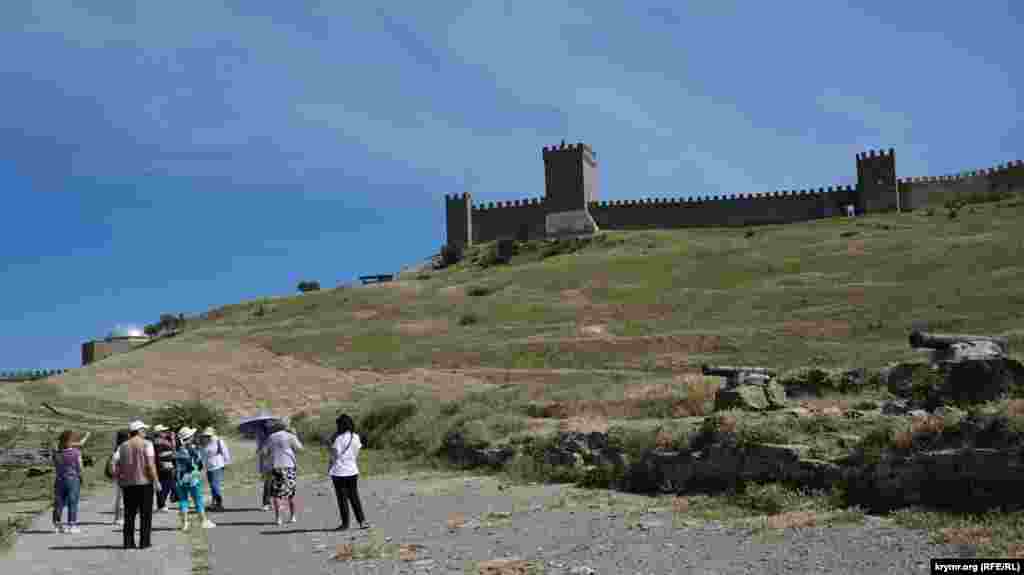 Ziyaretçiler gruppası qaleniñ tış divarı yanında