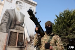 Боевик антиправительственного движения стоит у изуродованного портрета президента Сирии Башара Асада. Город Хама, 6 декабря 2024 г.