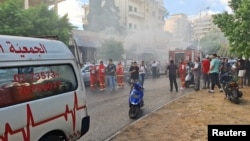 Fumul iese dintr-un magazin de telefoane mobile în timp ce membrii apărării civile se pregătesc să intervină în orașul Sidon, Liban, pe 18 septembrie 2024, la explozia unor dispozitive electronice. 