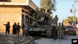 Опозициските борци стојат до тенк на сириската армија во градот Марат ел Нуман, југозападно од Алепо, Сирија, на 30 ноември 2024 година.