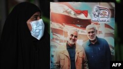 Ирактык аял ирактык колбашчы, маркум Абу Махди ал-Мухандис менен ирандык кол башчы, маркум Касем Сулайманинин сүрөтү тартылган көрнөктү көтөрүп турат. Багдад аба майданы. 2021-жылдын 2-январы.