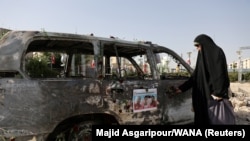 Израилдин аба соккуларынан кийин күйүп кеткен машиненин жанында турган ирандык аял. Тегеран, Иран. <br>