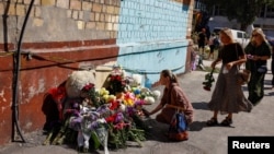 Femei din Kiev care depun flori la un memorial improvizat lângă un bloc unde ieri 22 de locatari au fost uciși de un atac cu rachete rusești.