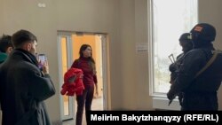 Orda.kz редакциясы есігінің сыртында тұрған қарулы полиция қызметкерлері мен заңгер Ольга Диденко (ортада). Алматы, 1 желтоқсан, 2025 жыл.