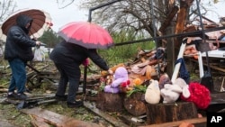 Femeile au pus flori lângă dărâmăturile unei case distruse, unde trei copii au fost uciși de un atac rusesc în regiunea Jitomir din Ucraina.